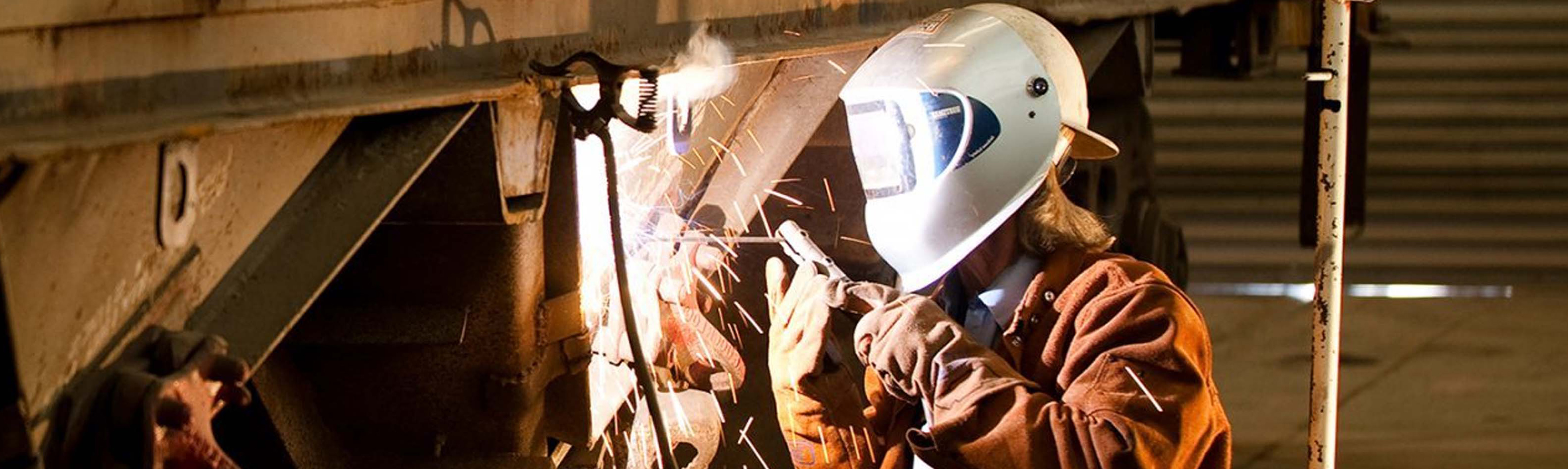 G&W employee wearing a welding helmet and repairing a railcar