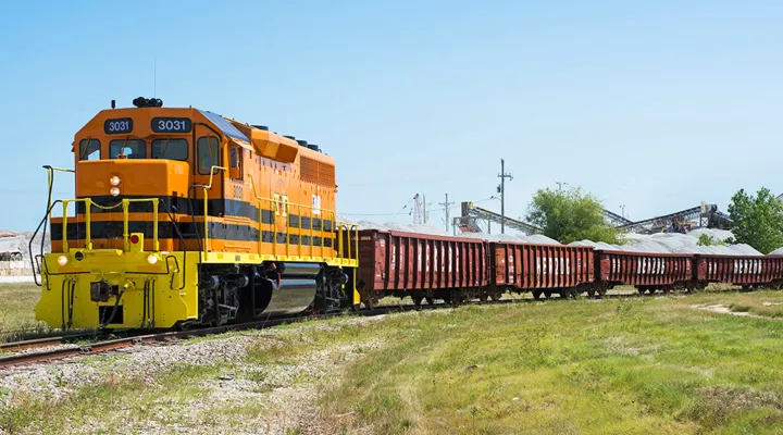 Orange and yellow train pulling freight railcars filled with construction material.