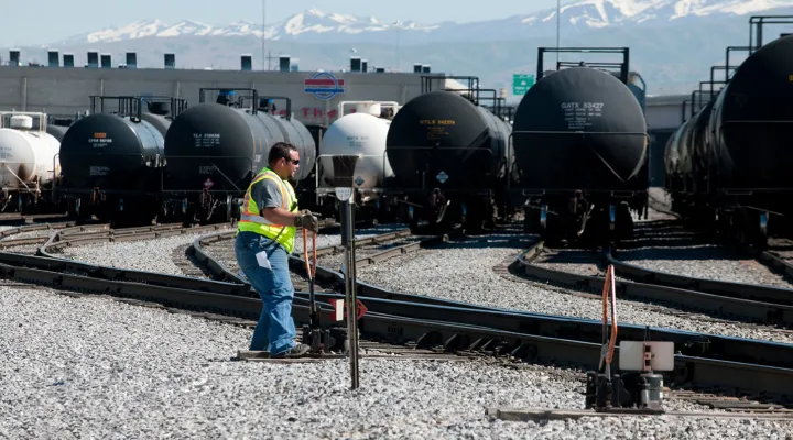 G&W employee wearing a high-visibility vest and sunglasses moving a track's direction in a railroad yard filled with tank cars