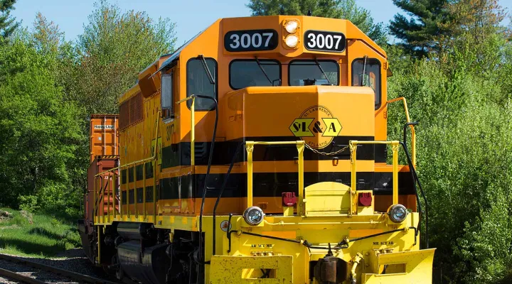 Train pulling freight railcars around a winding track with trees in the background