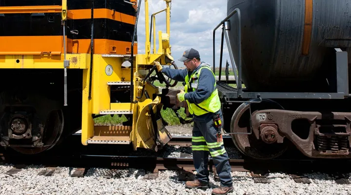G&W employee wearing high-visibility clothing, safety glasses, and a cap using tools on a traincar