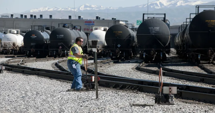 G&W employee wearing a high-visibility vest and sunglasses moving a track's direction in a railroad yard filled with tank cars